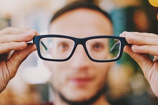 Man holding his glasses away from his face bringing the world into focus