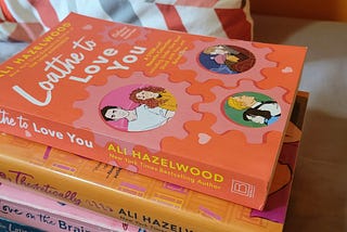 A stack of books by Ali Hazelwood, with the novella collection Loathe to Love You featured on top