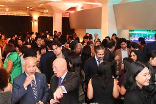 A crowd of people having drinks and in conversation in the lobby outside the main gala room. The crowd is very diverse and inclusive, with young and older adults, women and men, from the broadest definition of the Asian diaspora and non-Asian friends and family.