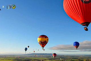 Vários balões de ar quente coloridos voando sobre a paisagem verde de Boituva em um dia ensolarado, com céu azul e algumas nuvens ao fundo. O balão vermelho à direita aparece em destaque, enquanto outros menores se espalham pelo horizonte.