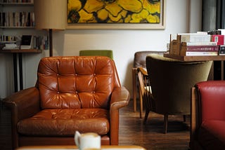 A brown leather club chair is the focus with a desk and other chairs in the background.