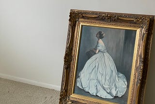A painting of a woman in a white evening gown with a gold frame is propped against a blank wall with a dirty sheet on the floor next to it.