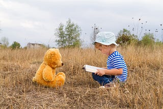 A child reading a story to her stuffed bear.