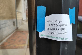 A white note taped to a black pole that reads What if you loved yourself as hard as you judge yourself? www.randomnoteproject.com