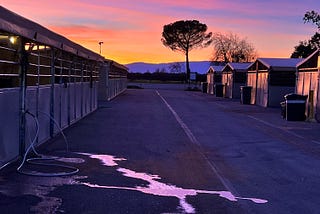 An orange, blue and gold Northern California sunset paints a barn aisle with color. Silouetts of trees and purple mountains in the background.