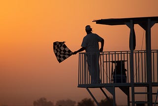 silhouette of man holding checkmark black and white flag against an orange evening light background