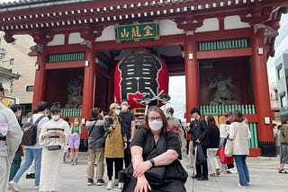 Picture of a woman in a black dress sitting in her wheelchair in front of a Japanese temple