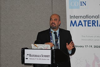 Ahmed wearing a black suit and standing in front of a podium.