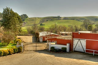 High vantage photo of the red Bucket Ranch with beautiful green hills in the background and a red barn in the foreground.