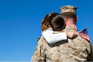 Veteran holding his daughter with her head tucked into his shoulder, holding an American Flag.