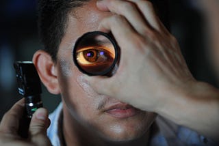 Picture of an optician examining an man’s eye with a magnifying lens