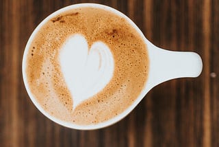 white coffee cup filled with coffee and a heart made of cream on top