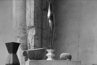Black and White photo of the 1926 Sculpture “Bird in Space” on a plinthy with some abstrtact objects beneath.