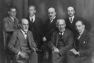 Black and white photograph of seven mature and older men in suits, sitting and standing