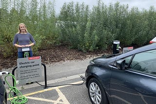 Grey electric vehicle charging at the Eden Project in Devon with a woman standing near the chargepoint.