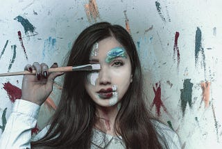 A woman covering her right eye with a paint brush.