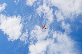 Red airplane viewed from far below against a blue sky with white clouds.