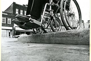 Mid-century photo of person in wheelchair navigating inaccessible sidewalk.
