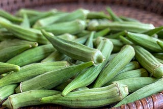 Fresh okra pods are spread on a brown basket.