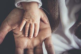 An adult hand representing a father against a child hand, representing parenthood.