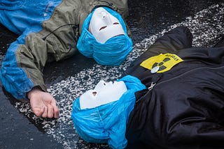 A photograph of two people lying on the ground, wearing white masks and with their heads wrapped in blue plastic.