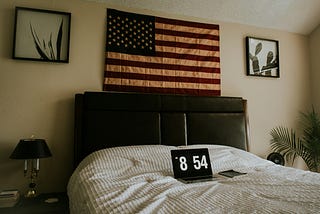 flag above bed headboard, laptop on bedsheets showing 8:45