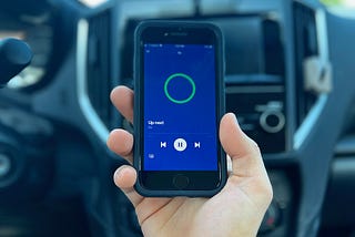 A hand holds up a phone displaying the DJ button on Spotify.