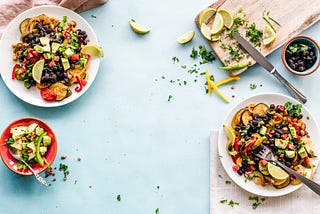 Three bowls of filled with fresh food and herbs and lime with a cutting board that has fresh lime and herbs prepped on it. There is also a small bowl filled with black beans.