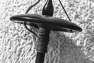 A wooden top-whirl drop spindle with yarn wound around it. It’s in black-and-white because it looked more artsy that way