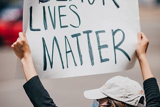 Masked white woman holding up a “Black Lives Matter” sign