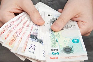 A man holding a fan of British pound notes for a cash transaction.