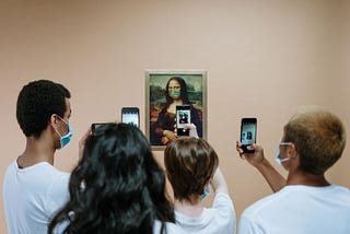 A group of people with medical masks takes a photo of a painting of the Mona Lisa, also wearing a medical mask.