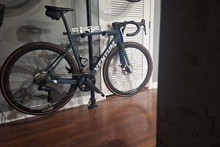 A sleek Ventum NS1 road bike with an aerodynamic design, displayed indoors on a rack, set against a backdrop of a wall and a louvered door.