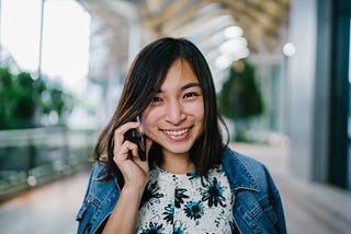 Woman calling on a mobile phone, looking in the camera, blue jacket white shirt with flower print, the woman is smiling and looks content, she’s outside. The picture accompanies a story by Katie on Medium about switching from iPhone to Samsung (from iOS to Android), what the reasons are for switching and the benefits of the new phone.