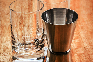 Two cocktail glasses with a shaker container placed on a wooden bar top