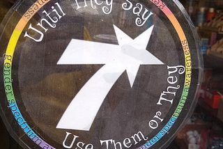 Circular sign on a cafe door, around the edges are rainbow colors and the text “Until they say, use them or they”
