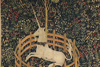 A tapestry depicting a unicorn wearing a collar and trapped by a small circular fence. Behind the unicorn, also in the fenced space, is a small tree. The ground is covered in wildflowers against a dark background.