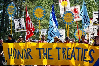 People stand behind a banner reading “Honor the Treaties” at a protest against Line 3.