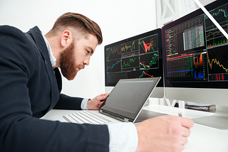 man studying crypto signal trade alerts on three computer screens