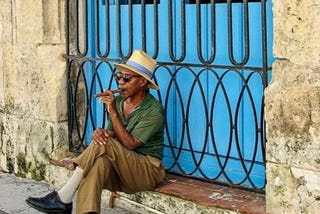 Cuban man smokes cigar on a step in front of a distinctive sky blue doorway