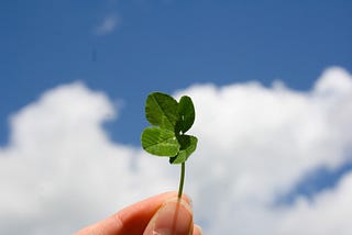 a hand holds a four leaf clover against the backdrop of a slightly cloudy sky