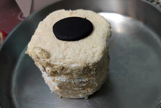 Japan cake, a nut-meringue based pastry dessert topped with a chocolate coin on a stainless steel plate