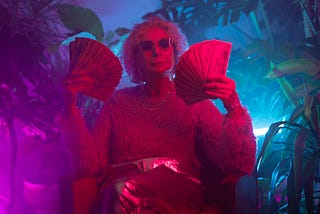 Older woman wearing sunglasses. Jungle background. She is sitting in a chair and fanning stacks of money.