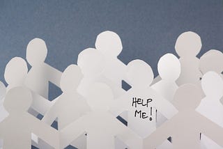 Rows of white paper people chains and one individual has the words Help Me written on it. Concept image for opioid overdose crisis.