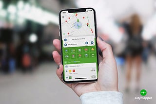 Someone is holding a smartphone which is displaying the landing page of the Citymapper app.