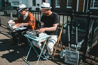 Two poets sitting at typewriters on the street