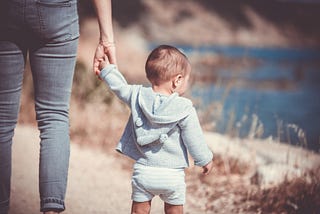 A woman walking holding the hand of toddler
