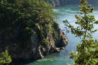 Steep cliffs descending down to green waters with a bridge off in the distance.