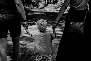 Parents holding their son hands.