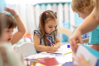 Kindergarten girl in class with friends, drawing with colored pencils